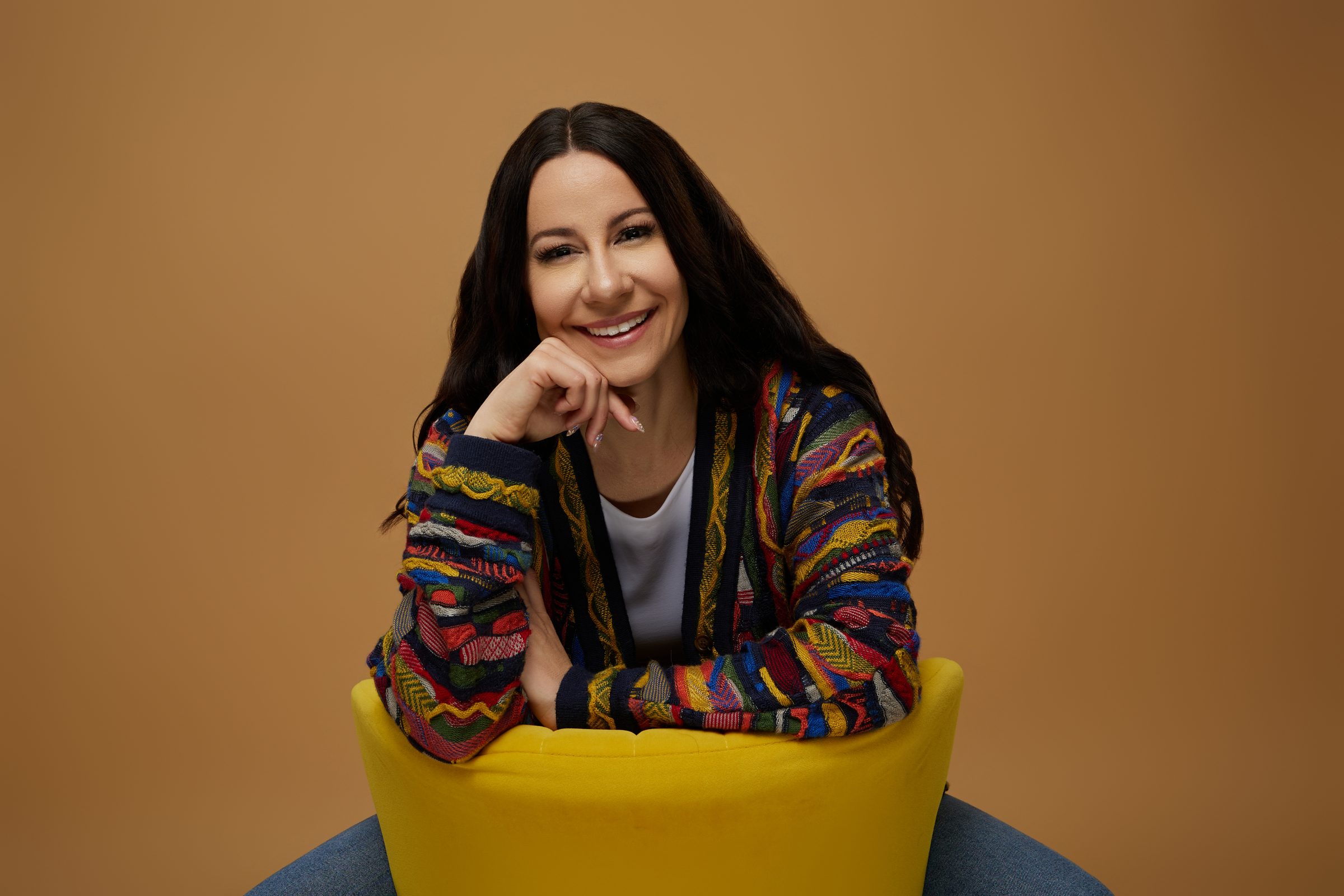 Bryanna Baptiste smiling, resting her chin on her hand while seated on a yellow chair