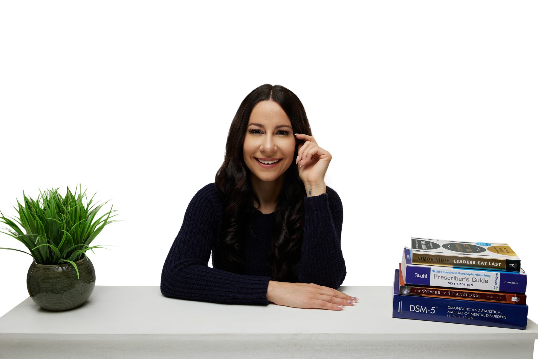 Bryanna Baptiste seated at a desk beside a plant and a stack of psychiatry books